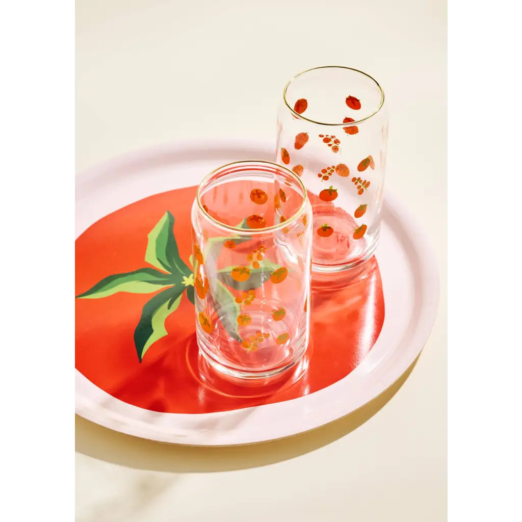 Two clear glass tumblers with fruit designs on a Tomato Gold Rimmed Soda Can Glass tray