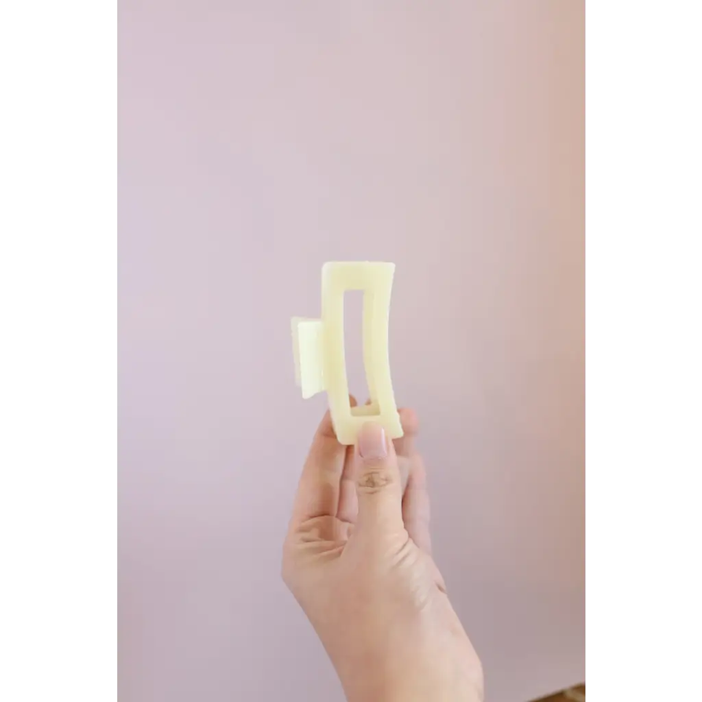 Hand holding two pale yellow butter sticks beside a Medium Size White Hair Clip