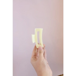 Hand holding two pale yellow butter sticks beside a Medium Size White Hair Clip