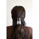 White plastic medium size hair clip holding dark hair in a chic ponytail style