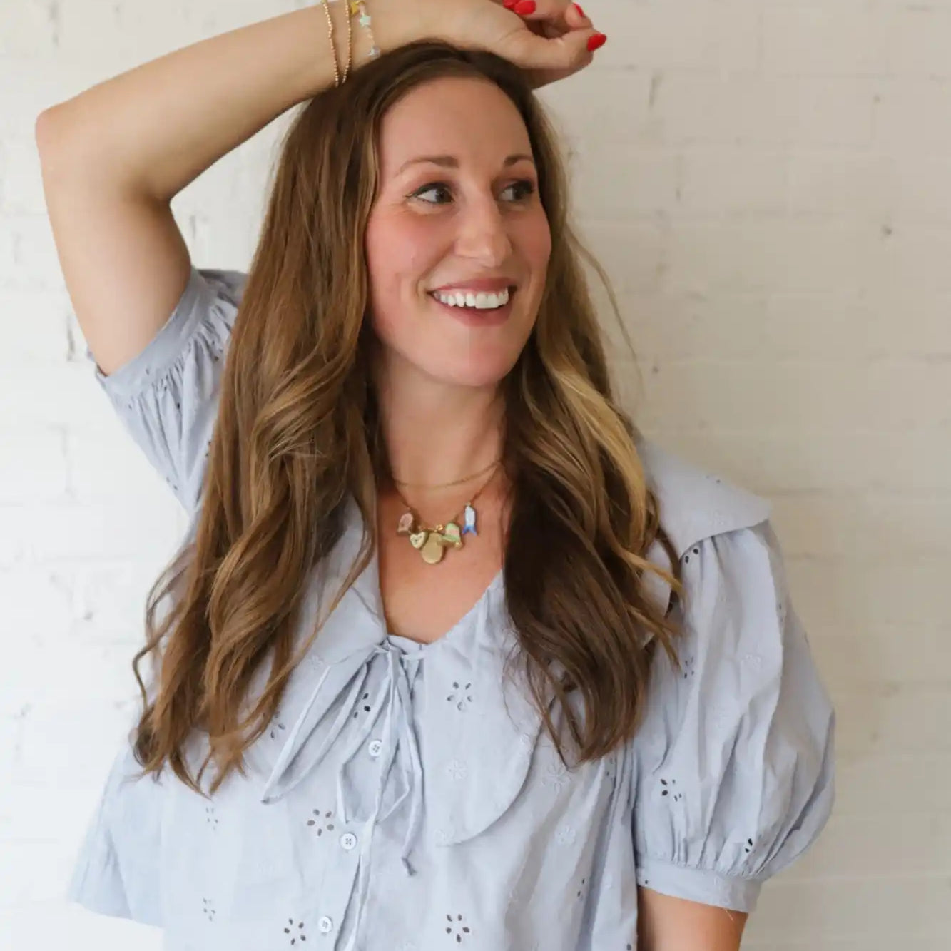 A woman with long brown hair, wearing a light blue eyelet blouse with a large collar and a gold statement necklace.
