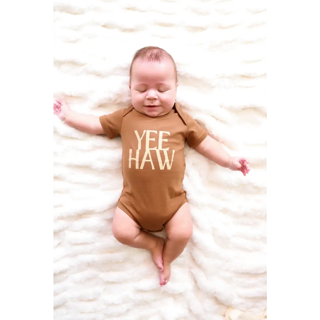 Baby in a brown organic cotton bodysuit with YEE HAW text on soft fabric