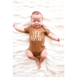 Baby in a brown organic cotton bodysuit with YEE HAW text on soft fabric