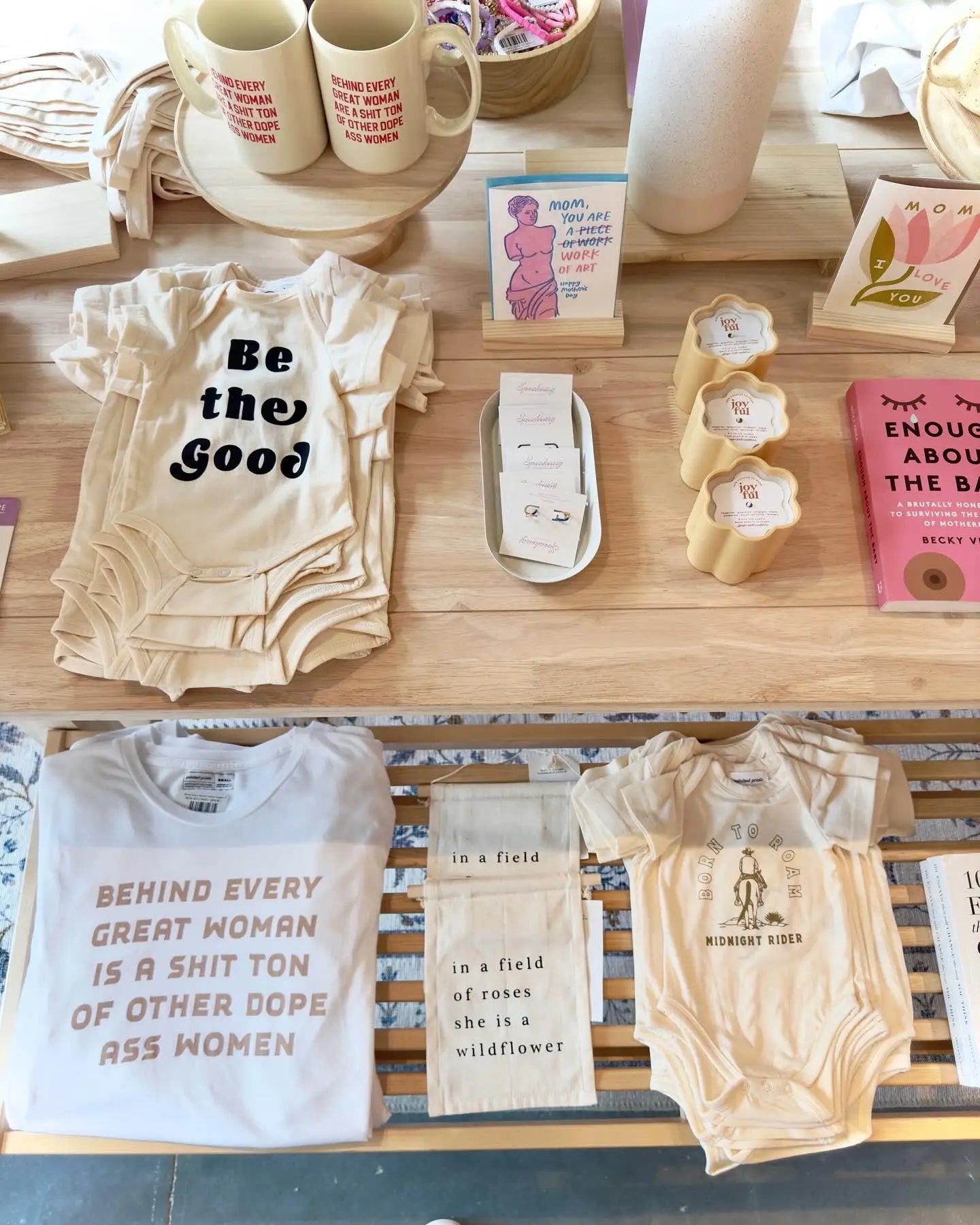 Feminist-themed baby onesies and mugs on wooden shelves at Polished Prints shop floor.