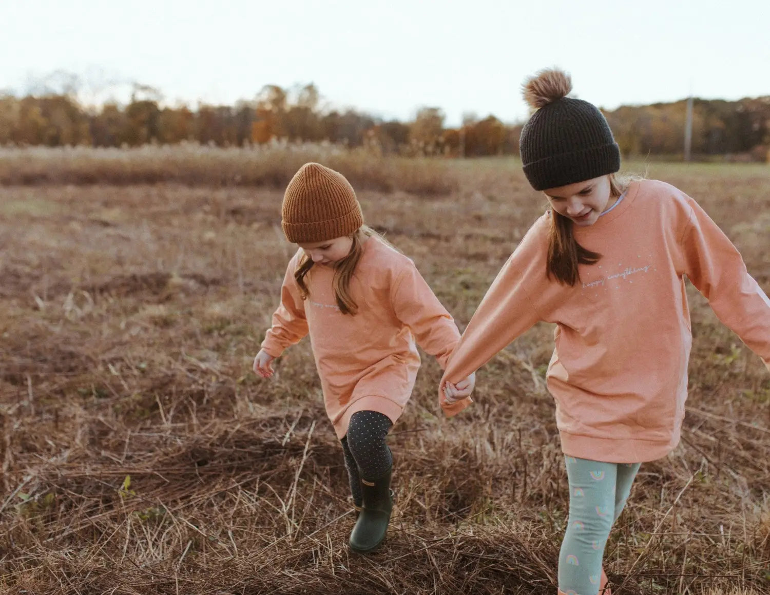Two kids in peach sweatshirts strolling through a field, perfect for Peace Signs Camp vibes.