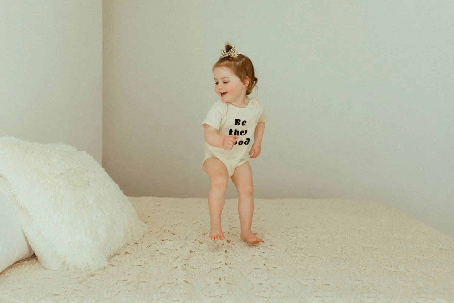 Toddler in a white cotton baby bodysuit with a playful grin, perfect for stylish newborns.