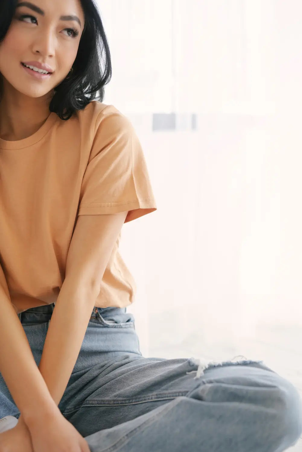 Person in a peach t-shirt and blue jeans showcasing cute womens clothes style.