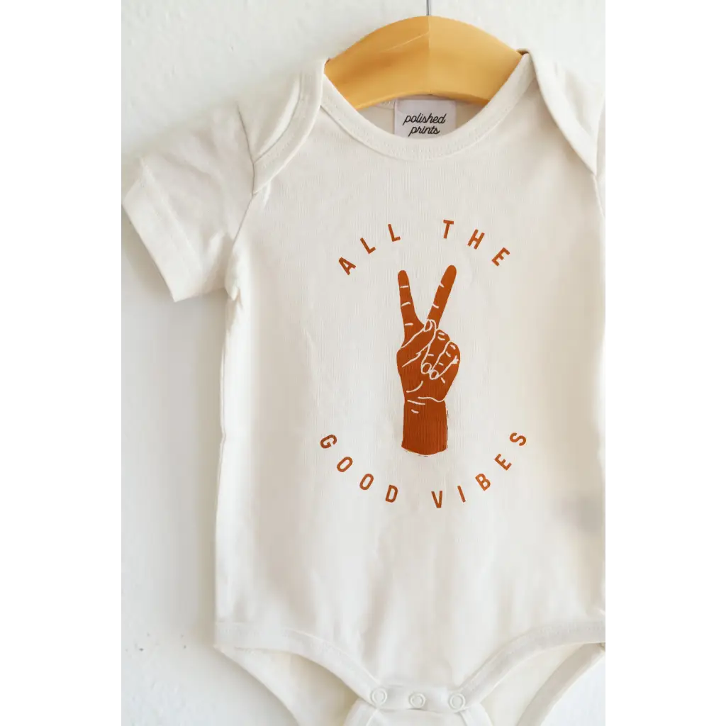 White baby onesie in organic cotton with orange Good Vibes text and peace sign graphic