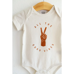 White baby onesie in organic cotton with orange Good Vibes text and peace sign graphic