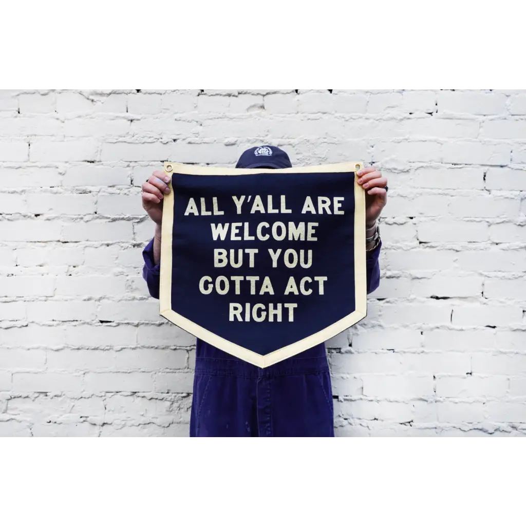 Navy blue pennant sign by Orleans artist Dr. Bob saying All Yall Are Welcome but You Gotta Act Right