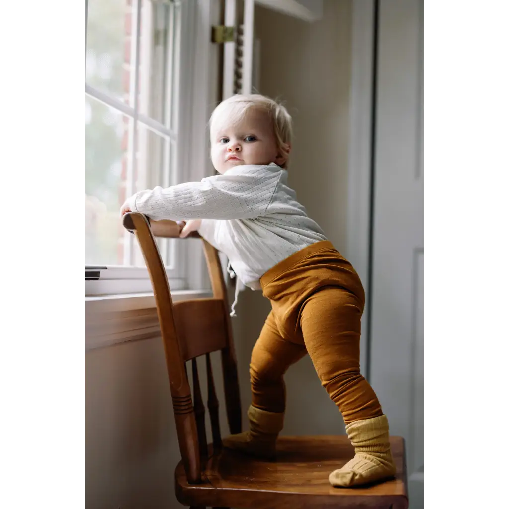 Toddler in white sweater and mustard pants, showcasing Baby Cathay Spice flexible lightweight leggings