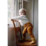 Toddler in white sweater and mustard pants, showcasing Baby Cathay Spice flexible lightweight leggings