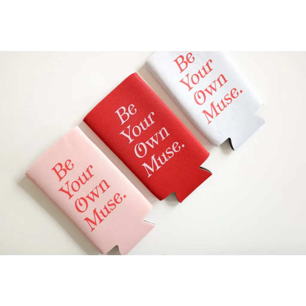 Three colorful printed seltzer koozies in pink, red, and white with Be Your Own Muse design