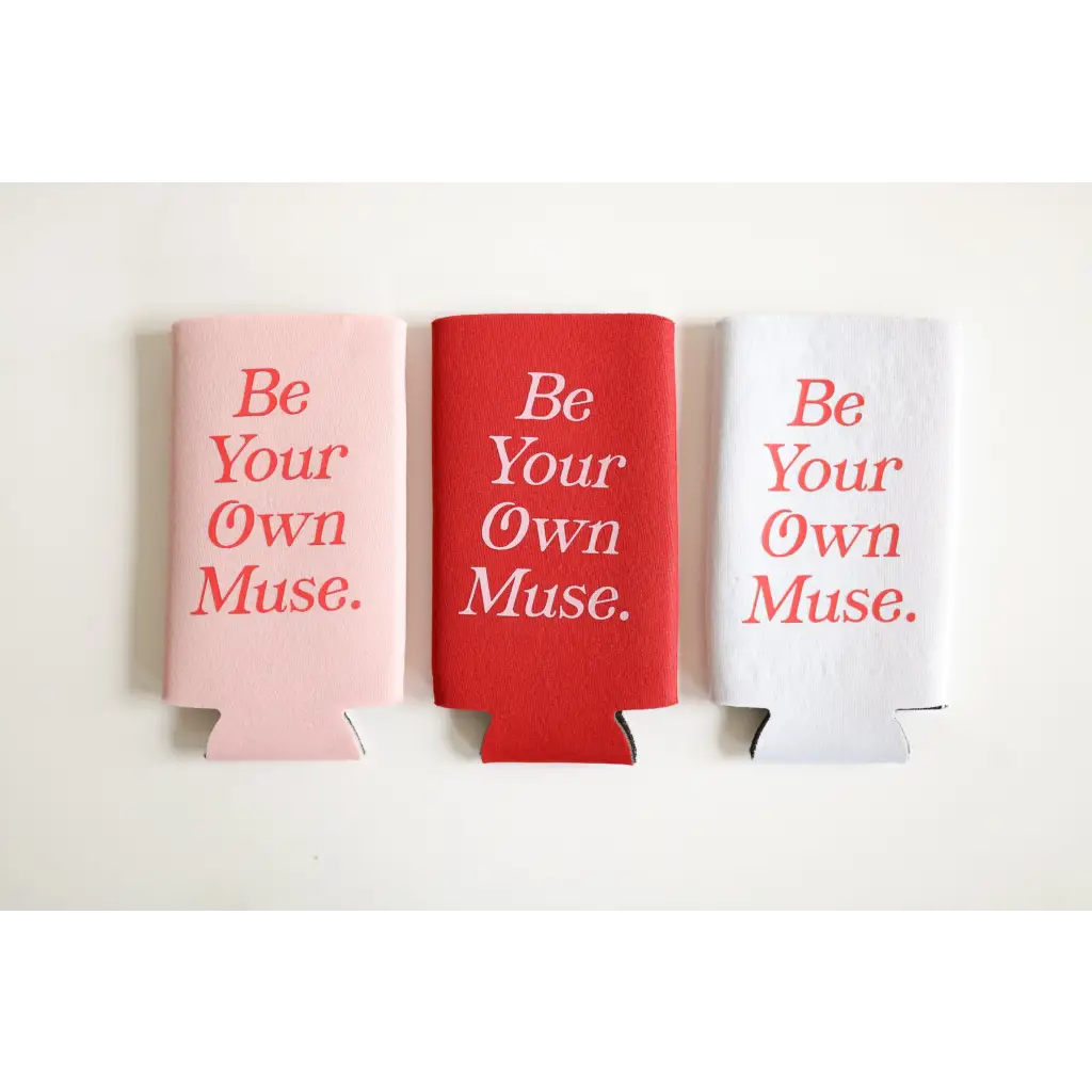 Three colorful printed seltzer koozies in pink, red, and white that say Be Your Own Muse