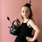 Young girl in a black witch costume with a black cat bucket bag for spooky fun