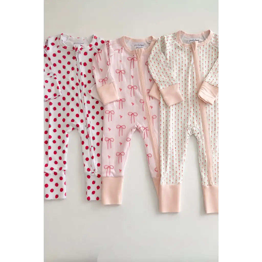 Three pink and white bamboo baby sleepers with polka dots, bows, flowers