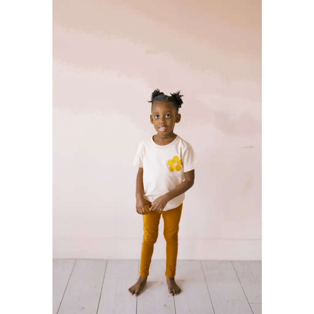 Child in white tee with yellow pocket and mustard pants, rocking Good Vibes Flexible Lightweight Leggings