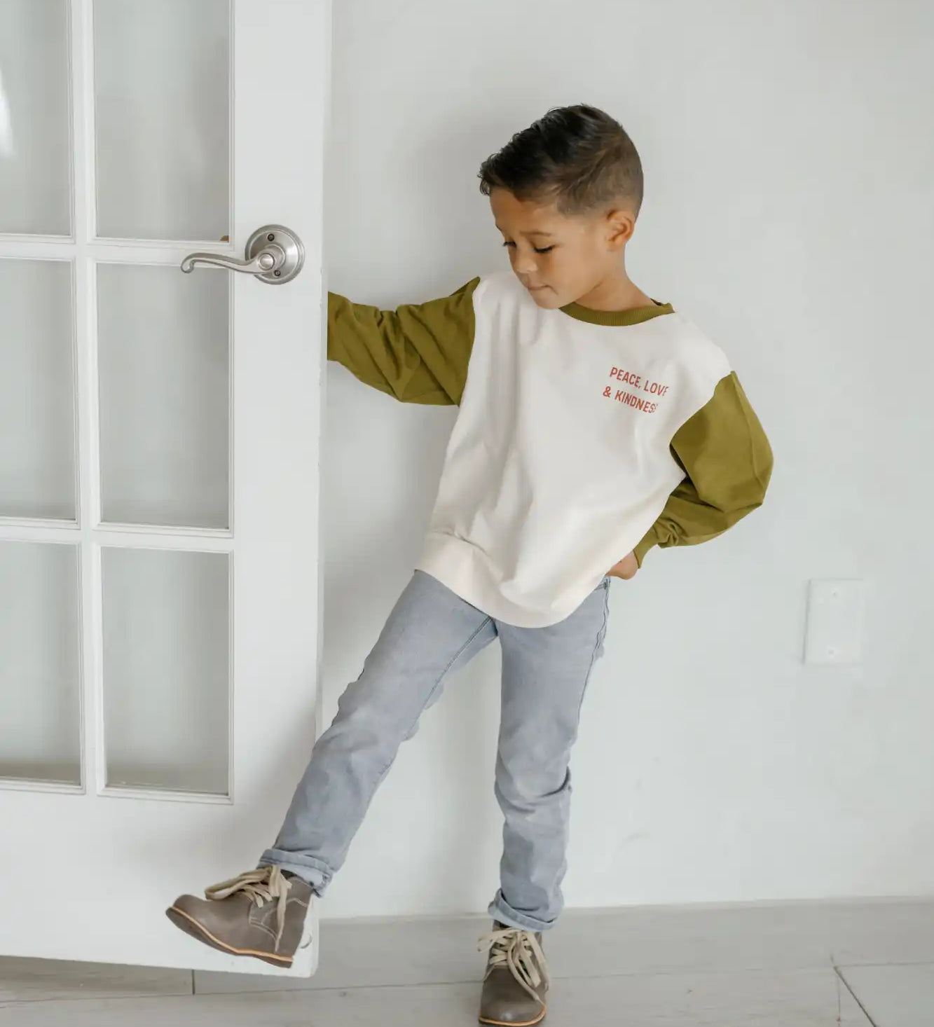 A child wearing a two-toned sweatshirt, jeans and sneakers in a playful pose.