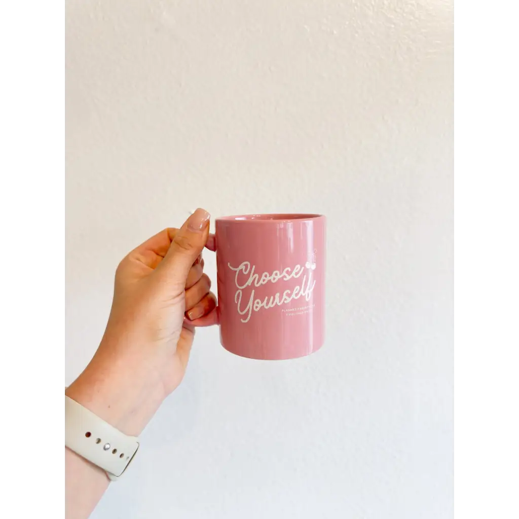 Pink 11oz coffee mug with Choose Yourself text held by hand, supporting Planned Parenthood