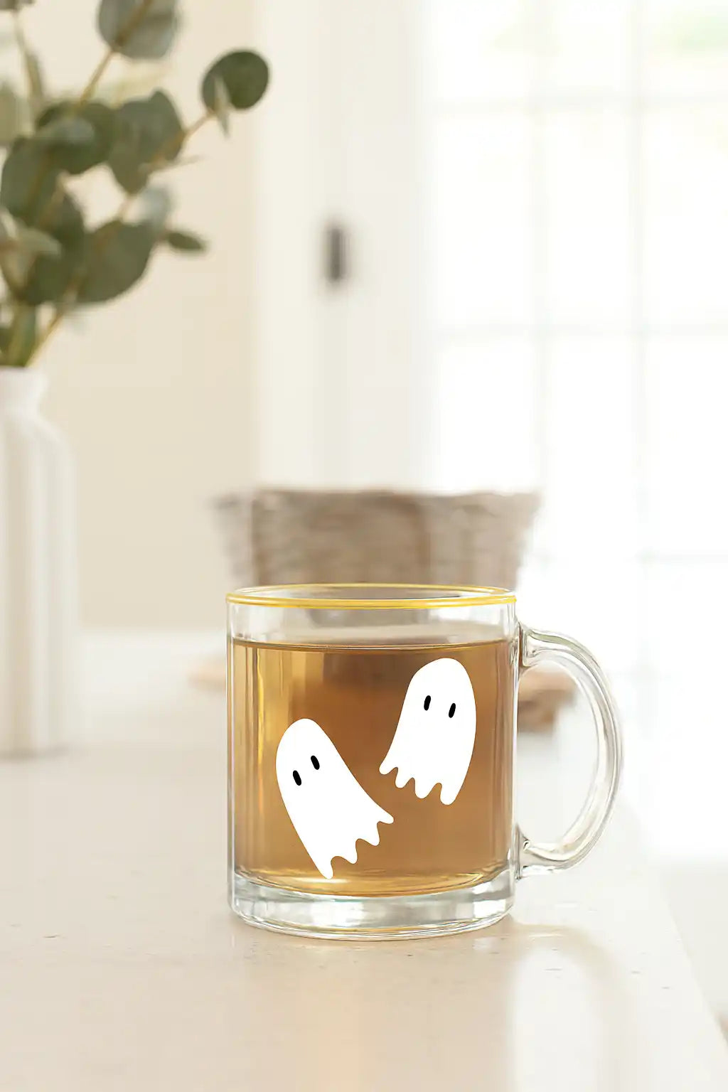 Clear glass mug with two white ghost decals, filled with a light brown beverage.