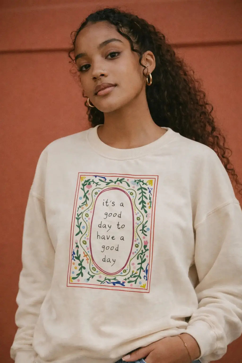 Cream-colored oversized sweatshirt with a colorful embroidered design featuring the phrase ’it’s a good day to have a good day’ framed by floral patterns.