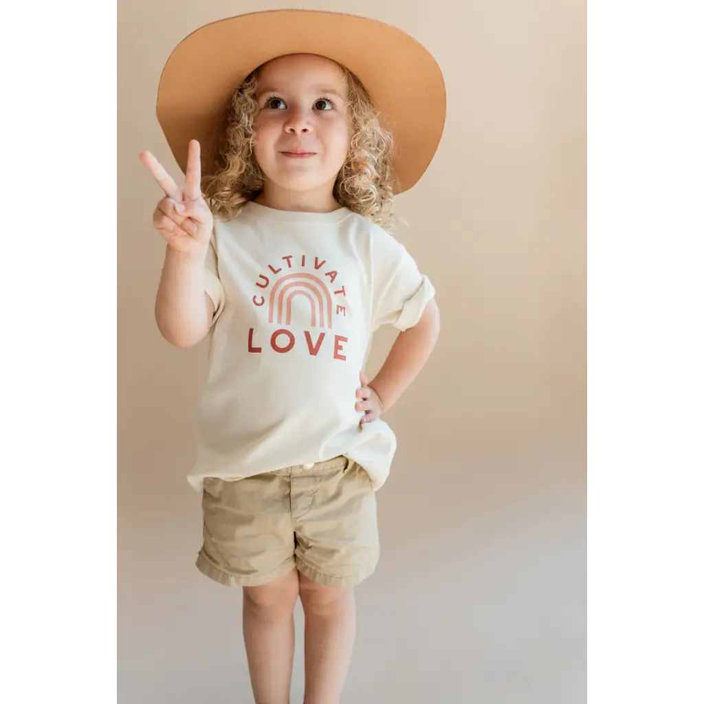 Kid rocking a Cultivate Love Organic Cotton T-shirt, peace sign, and cute hat