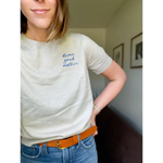 Woman wearing a beige T-shirt from the Damn Good Mother Sweater Tee collection