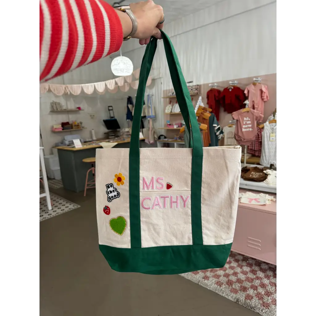 White canvas tote bag with green handles, colorful patches, and MS CATHY embroidery for craft bar party includes