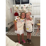 Two happy girls in birthday-themed shirts at the craft bar with a fun bar host