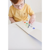 Young kid in yellow shirt with watercolor book and colorful prints, holding a brush pen