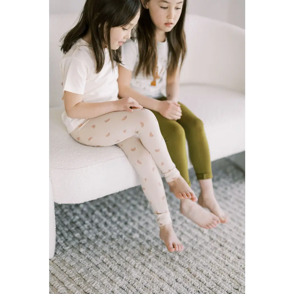 Two kids in casual wear on a couch showcasing Ditsy Rainbow Leggings by Polished Prints