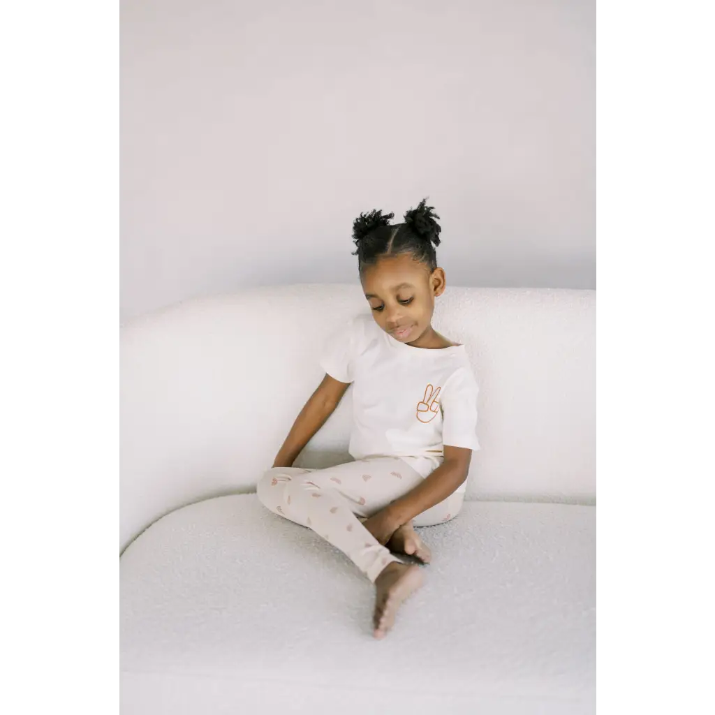 A child in a white t-shirt and light pants shows off Ditsy Rainbow Leggings with Peace Sign