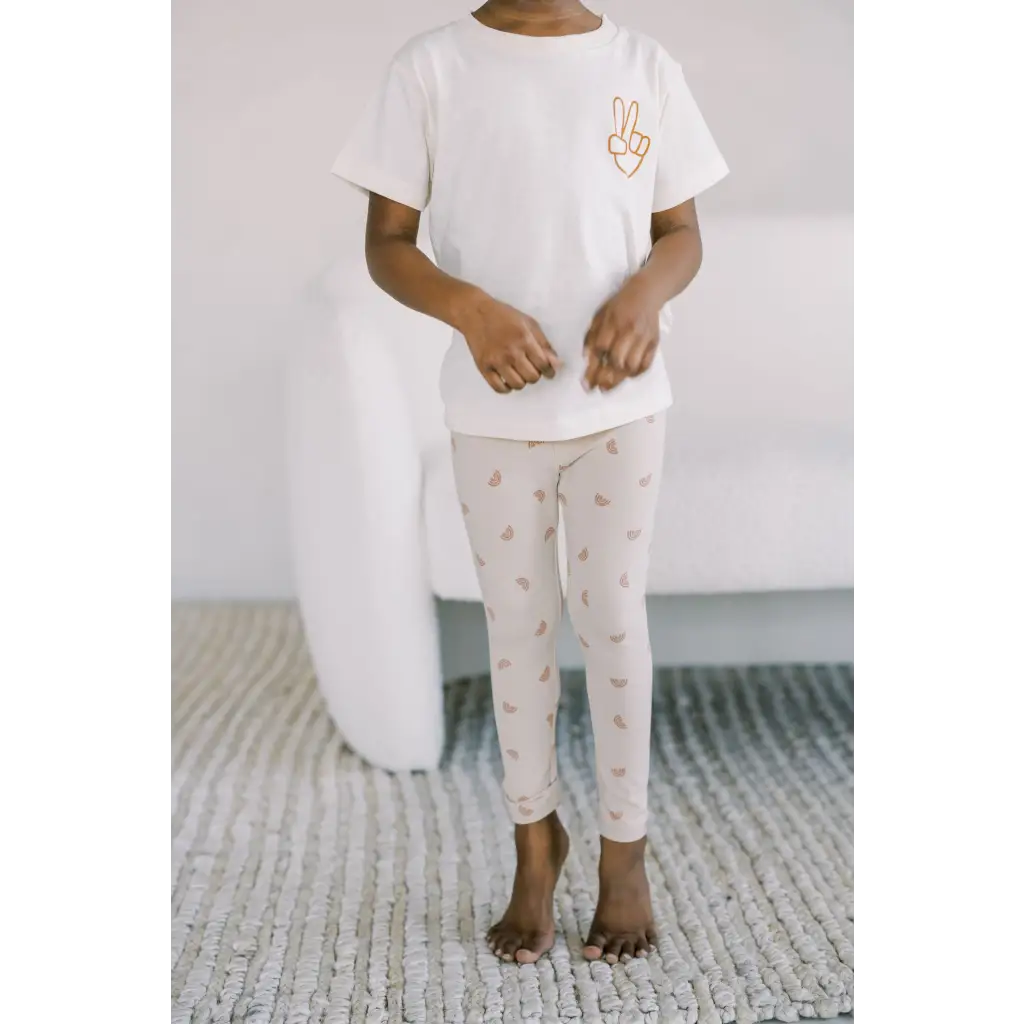 Kid wearing a white t-shirt with ditsy rainbow leggings and bare feet