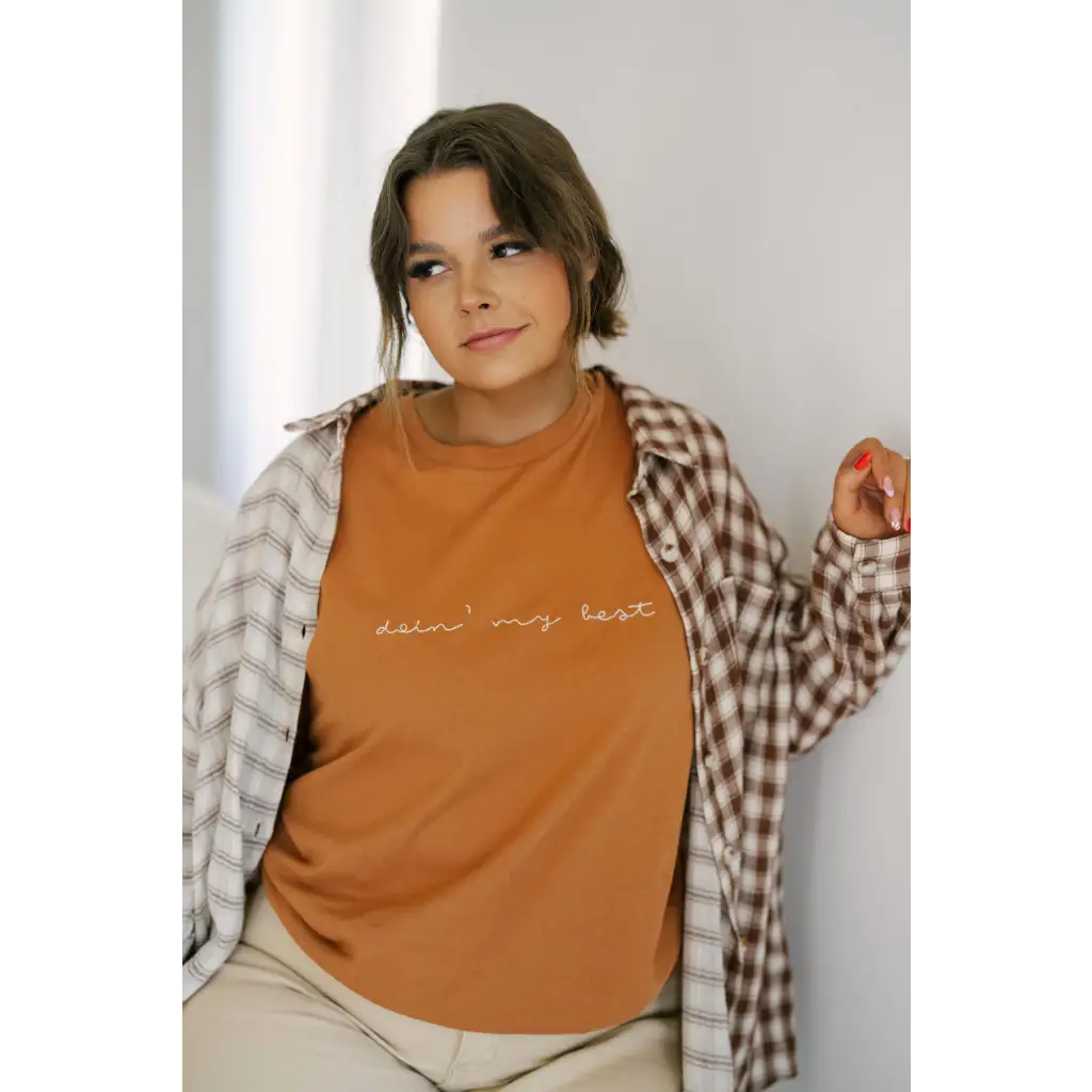 Orange t-shirt with cursive text under plaid flannel, featuring best embroidered details