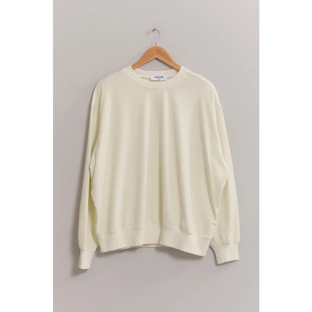 Cream-colored crew neck sweatshirt with drop shoulders hanging on a wooden hanger