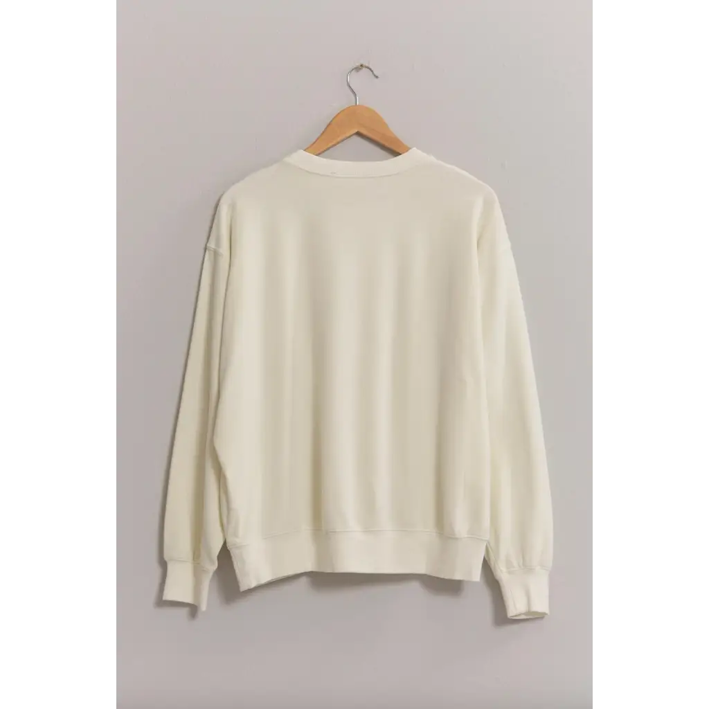 Cream-colored Drew Crew Neck Sweatshirt with drop shoulders on a wooden hanger