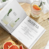 Open cocktail recipe book with grapefruit and drink next to Drinking for Two by Diana Licalzi