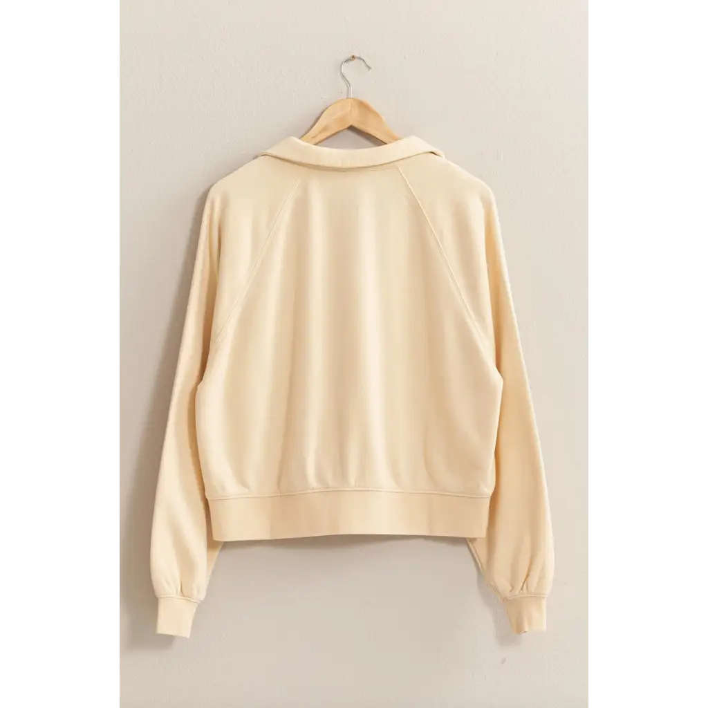 Cream-colored Eleanor Collared Raglan Sweatshirt hanging on a wooden hanger for stylish moms