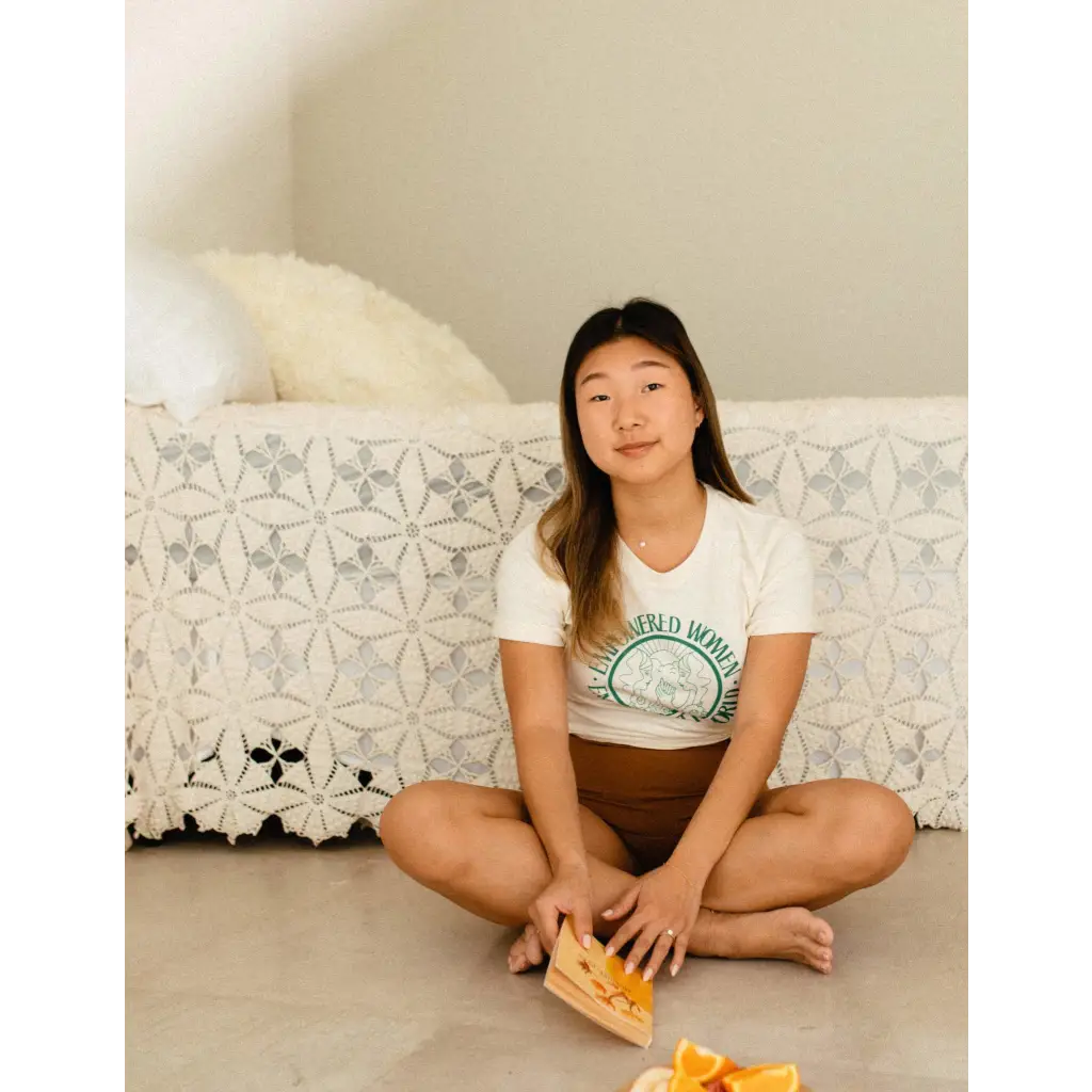 Person in Empowered Women Empower the World T-shirt by Polished Prints, holding orange snack