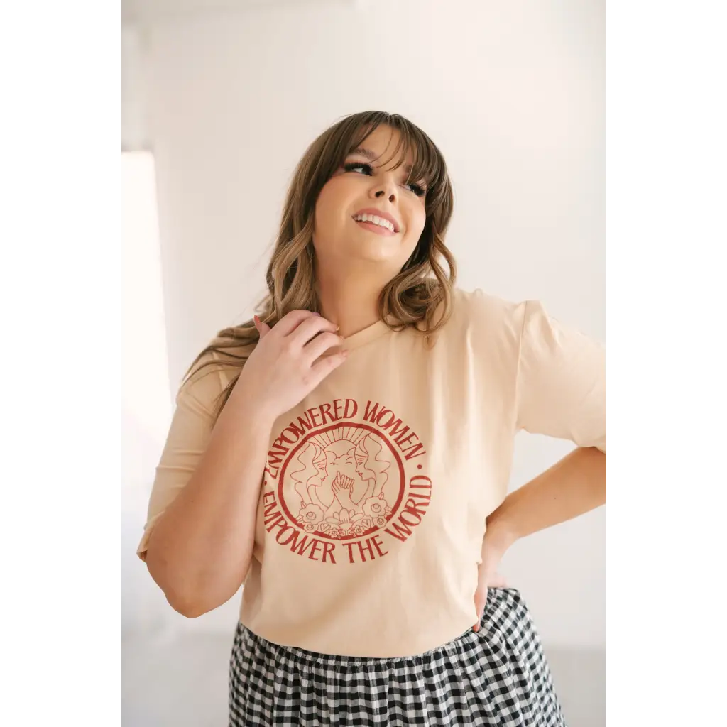 Beige Empowered Women graphic t-shirt with red design, styled with a checkered skirt