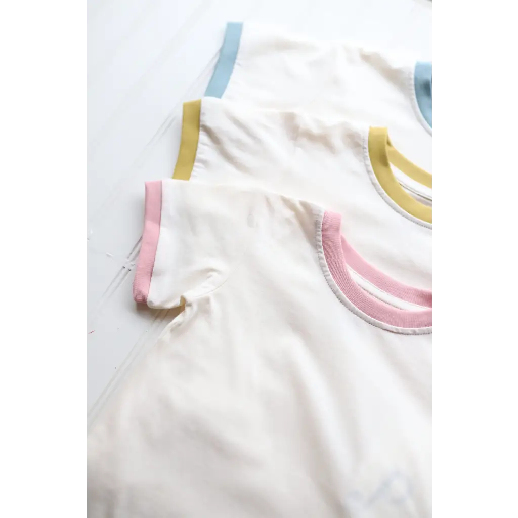 White fabric with pink, gold, and blue trim on a Retro Pastel Trim Everyday Ringer Tee for Kids