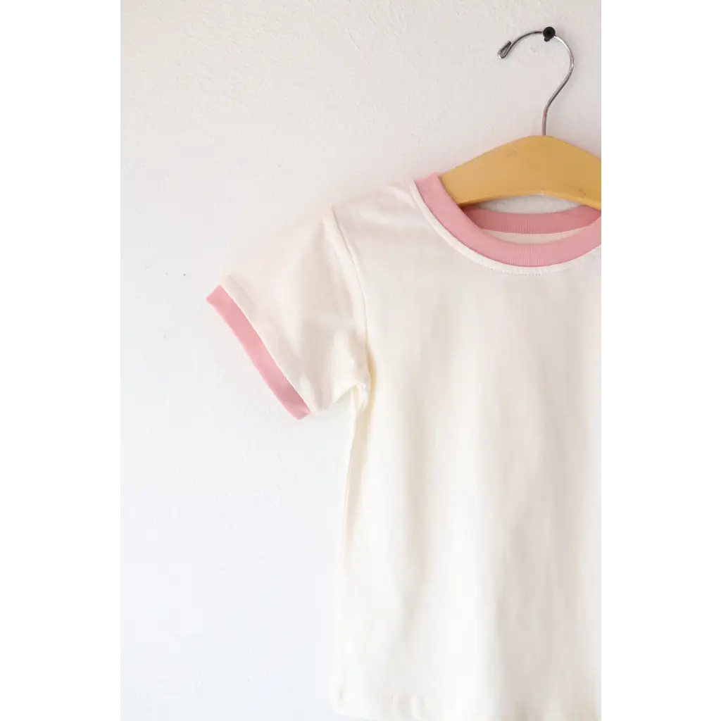 White everyday ringer tee with pink trim hanging on a wooden hanger for kids