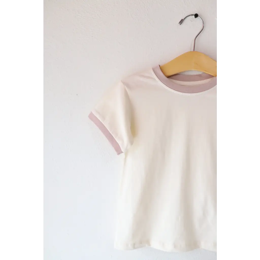 White Everyday Kids Ringer tee with pale pink trim hanging on a wooden hanger