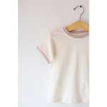 White Everyday Kids Ringer tee with pale pink trim hanging on a wooden hanger