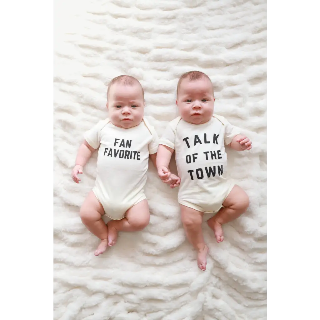 Two babies in Fan Favorite baby onesies relaxing on soft white fabric