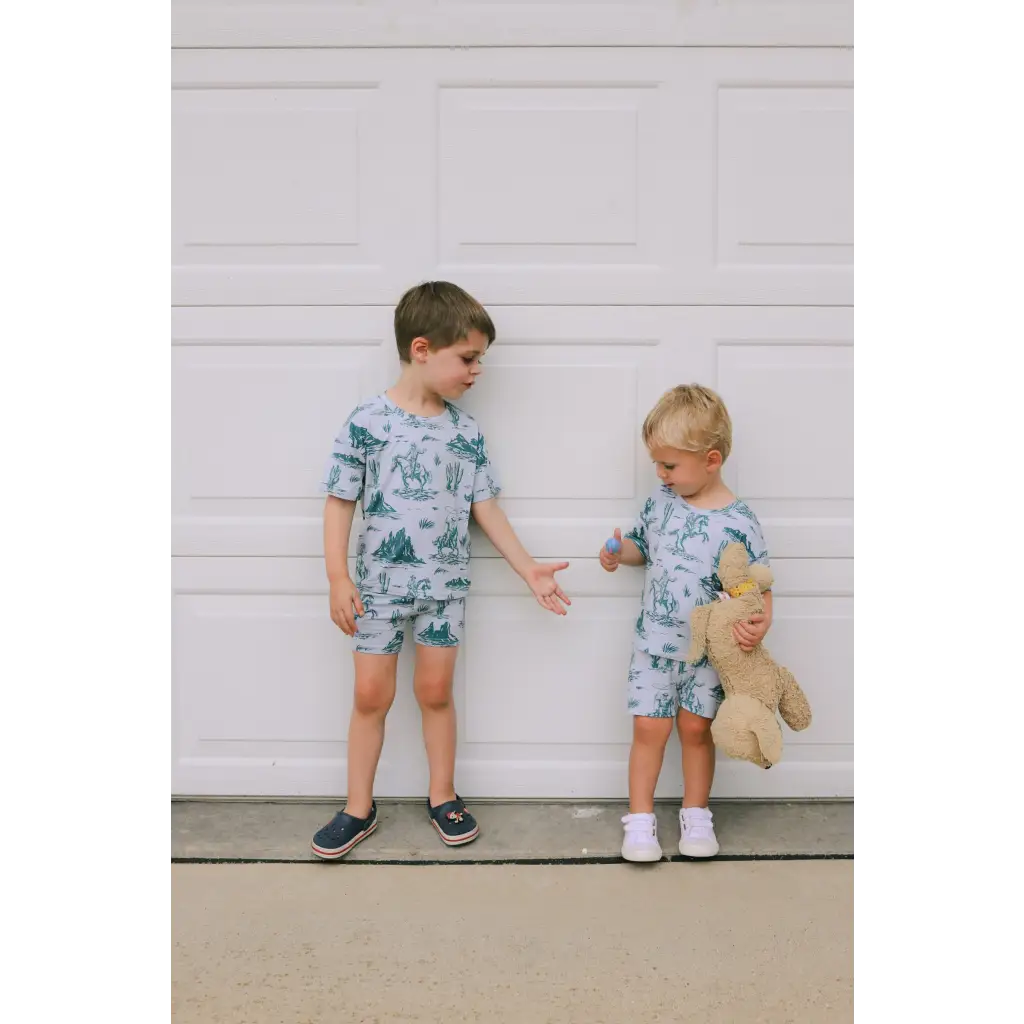 Two kids in matching blue pajamas with a teddy bear, showcasing the Rodeo Short Set