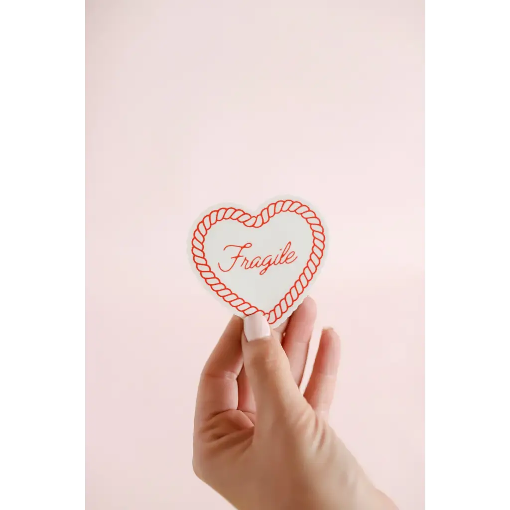 Hand holding a heart-shaped fragile sticker in a rope border for soft girl vibes