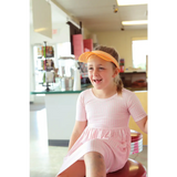 Child in a pink twirl dress and orange visor sits on a stool for Gingham All Day Twirl