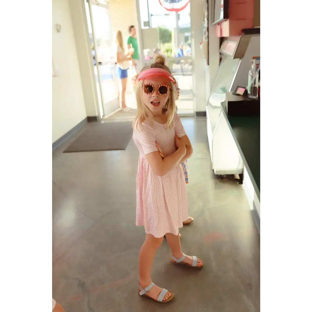 Child in pink Gingham dress, stylish sunglasses, and sandals for fun summer vibes