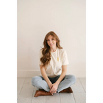 Person in light blue jeans and White Good Vibes Peace Embroidered Tee sitting cross-legged